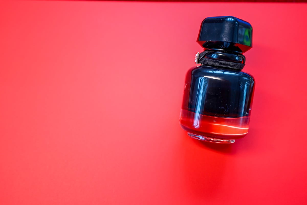 Black perfume bottle with red liquid on a bold red background